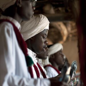 Khamlia gnaoua music Profile view of three individuals wearing white turbans and traditional attire, deeply focused and holding metallic objects, likely engaged in a cultural or religious ceremony.